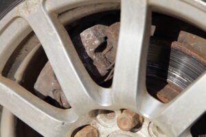 A close-up of a rusty brake disc through the spokes of a wheel.