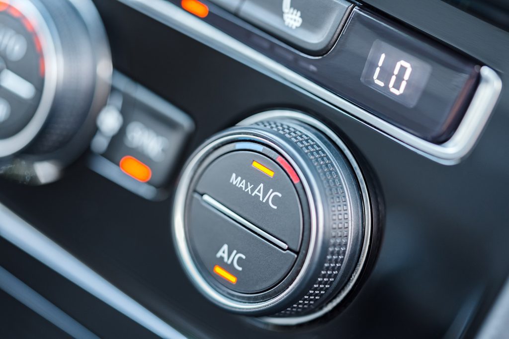 A black knob on a car's dashboard for the air conditioning, with a yellow light indicating it's on max AC.