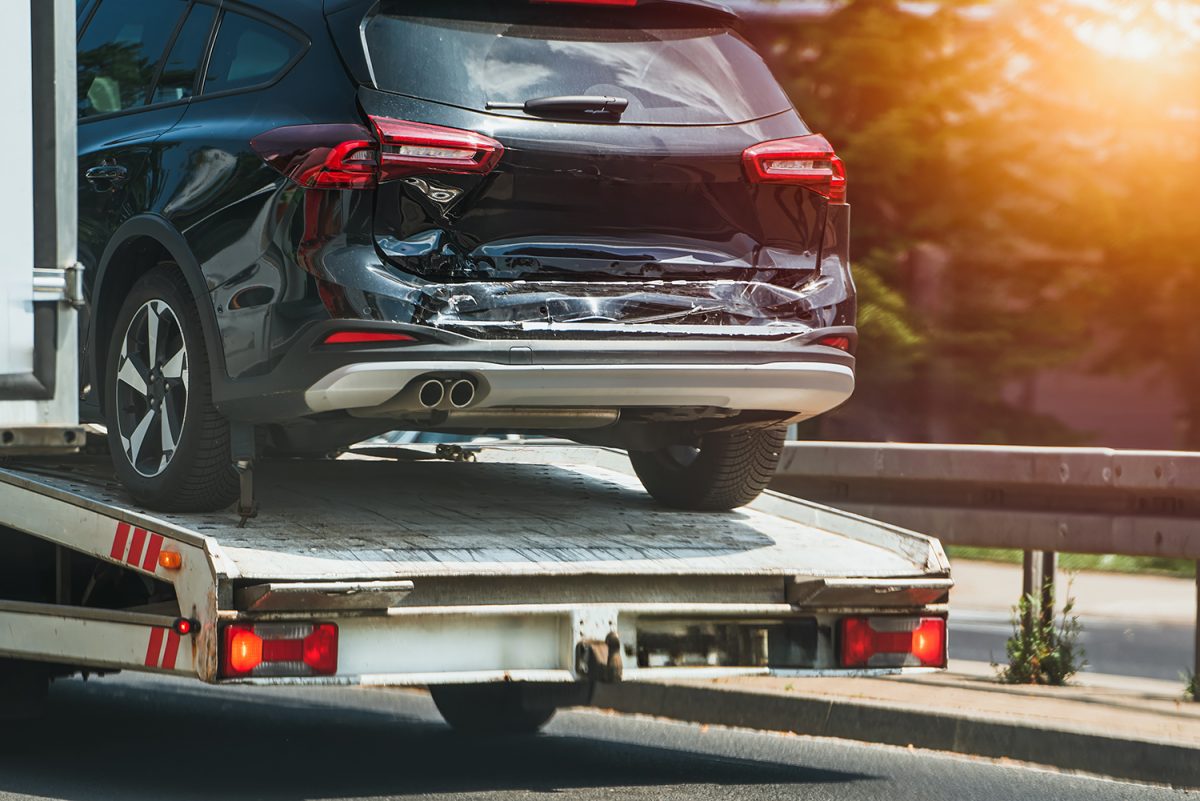 A black car on the bed of a truck with a large dent in the back.